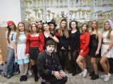 Na szkolnym korytarzu stoi duża grupa licealistów w kostiumach Halloween. Przed grupą kuca chłopak w białej masce.