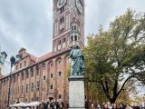 Grupa młodzieży dookoła pomnika Mikołaja Kopernika w Toruniu, w tle Ratusz Staromiejski