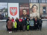 Grupa uczniów w zimowych ubraniach stoi przed wejściem do teatru. Za nimi afisze reklamujące spektakle teatralne