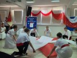 Uczniowie w strojach galowych z czerwonymi szarfami tańczą z flagą Polski