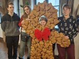 Uśmiechnięta dziewczyna w fotobudce w kształcie dużego piernikowego ciastka. Obok niej troje uczniów