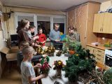 Grupa uczniów i kobieta przy długim stole. Na stole stroiki bożonarodzeniowe, gałęzie, igliwie, bombki