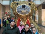 Pięcioro dzieci stoi przed dużą świąteczną dekoracją w postaci złotego podświetlonego misia