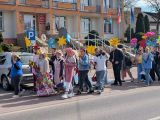 Uczniowie w barwnym korowodzie maszerują ulicami miasta. Z przodu uczniowie w barwnych wiosennych przebraniach. W tle...