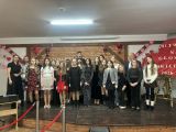 Grupa dzieci w barwnych strojach stoi na scenie podczas wręczenia nagród konkursu wokalnego, a po prawej stronie na...