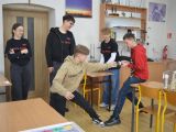 Pośrodku sali lekcyjnej, między ławkami dwóch chłopców próbuje rozerwać magnes. Obok stoi troje licealistów w czarnych...