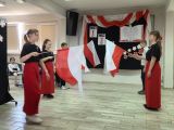 Trzy uczennice i dwóch uczniów z flagami Polski w dłoniach. Dziewczynki ubrane są w czarne koszulki i długie czerwone...
