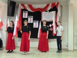 Trzy dziewczynki w czerwonych długich spódnicach i chłopiec w galowym stroju stoją z flagami Polski w dłoniach
