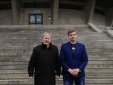 Przed schodami stoi starszy mężczyzna z siwymi włosami i uczeń z liceum w granatowej marynarce z blond włosami.