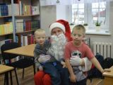 Dwóch chłopców ze szkoły podstawowje siedzi na kolanach św. Mikołaja. W tle regały z książkami.