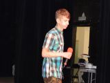 Chłopak w koszuli w kratę stoi na scenie, w ręku trzyma mikrofon.