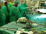 Grupa uczniów liceum w zielonych strojach chirurgicznych stoi przy stole opareacyjnym z narzędziami.
