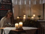 Uczennica liceum w okularach siedzi przy stole i czyta książkę. Na stole stoją dwie zapalone świece.