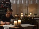 Uczeń liceum w okularach siedzi przy stole i czyta książke. Na stole stoją dwie zapalone świece.