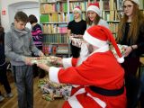 Uczeń szkoły podstawowej odbiera prezent od św. Mikołaja. Obok stoją trzy licealistki w czapkach św. Mikołaja.