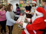 Uczennica szkoły podstawowej odbiera prezent od św. Mikołaja. W tle inne dzieci i dorośli.