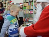Uczeń szkoły podstawowej odbiera prezent od św. Mikołaja. W tle dwie licealistki w czapkach św. Mikołaja.