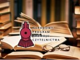 Księżki rozłożone na stole, na nich leżą okulary. W tle regały z książkami.