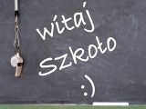 Na czarnej tablicy szkolej biały napis "Witaj szkoło :)".