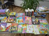 Na stole leżą książki. Jeden stos książek leżących jedna na drugiej, obok kilka książek stojących pionowo.