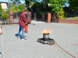 Uczeń liceum w czerwonej koszuli w czarną kratę w okularach gasi ogień gaśnicą.