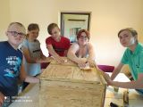Pięcioro ucznów klasy VI-VII SPUZ odnawiają szafkę drewnianą leżącą na stole.