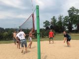 Sześciu chłopców z liceum odbija piłkę siatkową na piaszczystym boisku. Po środku boiska rozciągnięta siatka.