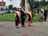 Troje uczniów liceum stoi ze sztandarem. W tle granitowy pomnik Władysława Łokietka.