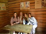 Trzy uczennice liceum wraz z kobietą w okularach siedzą przy stole w drewnianej chacie.