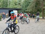W lesie grupa licalistów jadących na rowerach.
