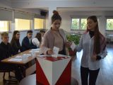 Dwie uczennice liceum stoją za urną do głosowania i wrzucają do niej kartki.