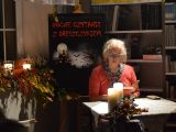 Kobieta w okularach czyta ksiązkę przy stoliku. Na stoliku stoją zapalone świece.