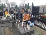Dwoje uczniów liceum, chłopak i dziewczyna, zapalają znicz na grobie nauczyciela na cmentarzu.