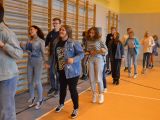 Duża grupa uczniów liceum tańczy w parach belgijkę na sali gimnastycznej.