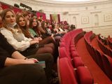 Grupa uczniów liceum siedzi w jednym rzędzie, w czerwonych fotelech na widowni teatru.