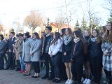 Duża grupa uczniów liceum stoi na dziedzińcu szkolnym. Wszyscy ubrani są w kurtki.
