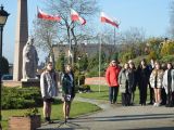 Dwie uczennice stoją przy mikrofonach obok pomnika Władysława Łokietka. Z boku stoi grupa licealistów.