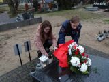 Dwoje licealistów składa kwiaty i zapala znicz na pomniku na cmentarzu.