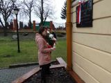 Dwoje licealistów składa kwiaty i zapala znicz pod granitową tablicą, która znajdujesię  na ścianie budynku.