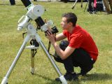 Uczeń liceum kuca na trawniku przy teleskopie. Licealista obserwuje przez teleskop niebo.