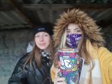Dwie uśmiechnięte uczennice liceum ubrane w czarną i żółtą kurtkę trzymają kartonową skarbonkę.