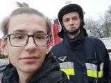 Trzech uczniów liceum  w okularach  stoi obok mężczyzny w stroju trażackim.