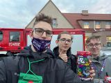 Trzech uczniów liceum stoi obok siebie na tle wozu strażackiego.