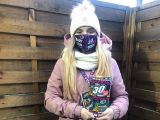 Uczennica liceum ubrana w różową kurtkę stoi i trzyma tekturową skarbonkę.