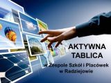 Na niebieskim tle wyciągnięta ręka w stronę kilku monitorów po lewej stronie. Na dole m.in. napis "Aktywna tablica".