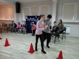 Kobieta trzyma za rękę uczennicę szkoły podstawowej, obie przechodzą między pachołkami.