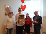 W jednym rzędzie stoją: kobieta, uczeń liceum trzymający drewniane pudełko, uczennica liceum, uśmiechnięty mężczyzna.