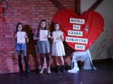 Na sceni, w rzędzie stoją trzy uczennice szkoły podstawowej. W rękach trzymają dyplomy.