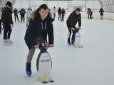 Dwóch uczniów liceum jeździ na łyżwach, opierają się o plastikowe pingwiny. W tle na łyżwach jeżdżą inni uczniowie.