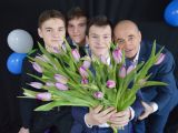 Trzech uczniów liceum i mężczyzna stoją w grupie. Przed sobą trzymają bukiet tulipanów. Wszyscy są w garniturach.
